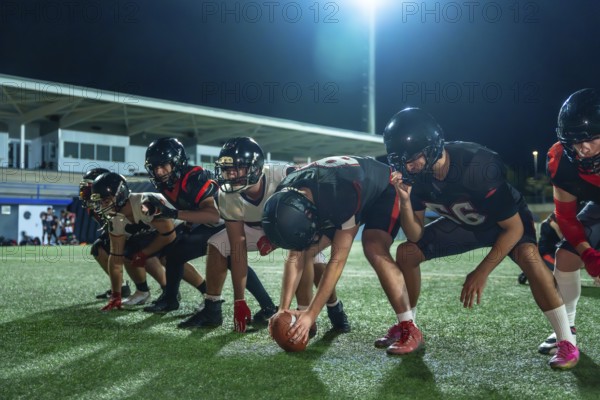 American football players in full uniform and helmets lining up on the green grass field at night,