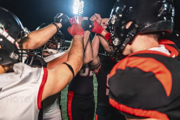 American football players huddling on the illuminated field, placing their hands together in the