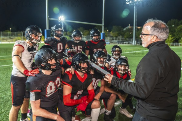 American football coach discussing strategy with his team of players in uniform and helmets during