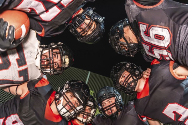 American football players wearing helmets and uniforms. Gathering in a huddle. Sharing a moment of