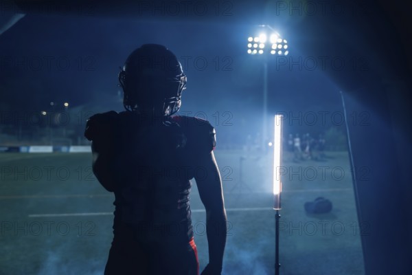 Football player standing in silhouette, ready to enter the stadium field at night, stadium lights