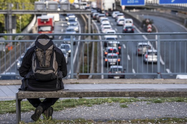 Man sitting on a bench, looking at the traffic jam on the A40 motorway, Ruhrschnellweg, in the city