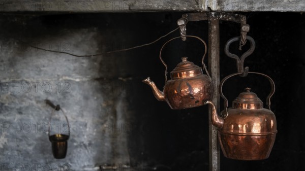 Alte Kupferkessel, die an Haken in einer rustikalen Küche hängen, historischer Bauernhof und