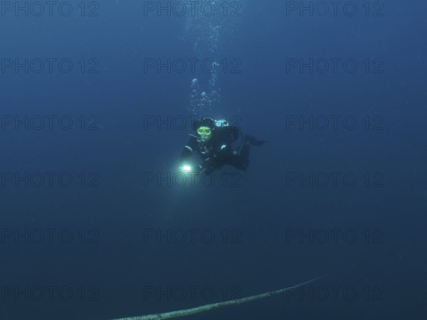 Ein Taucher mit Lampe steigt aus der dunklen Unterwasserwelt auf, einem Seil folgend. Tauchplatz