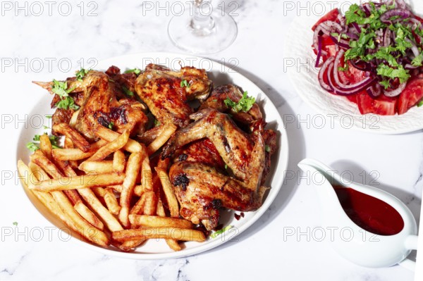 Delicious barbecue chicken wings, with French fries, salad and a refreshing drink, at a cozy table,