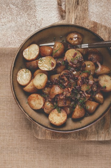 A bowl of perfectly roasted potatoes garnished with fresh herbs and caramelized onions sits on a