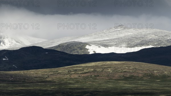 Blick auf schneebedeckten Berggipfel und baumlose Landschaft, dramatische Wolken, Pilgerweg