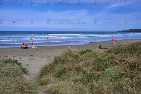 Rettungsflaggen am Strand mit grasbewachsenen Dünen und leichten Wellen im Meer, Kaka Point, Clutha