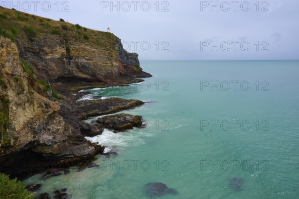 Dramatische Küstenlandschaft mit steilen Klippen Leuchturm und grünlich-blauem Meer unter einem