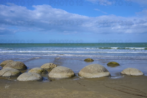 Mehrere runde Felsen an einem Sandstrand mit Blick auf das Meer und bewölkten Himmel, Moeraki
