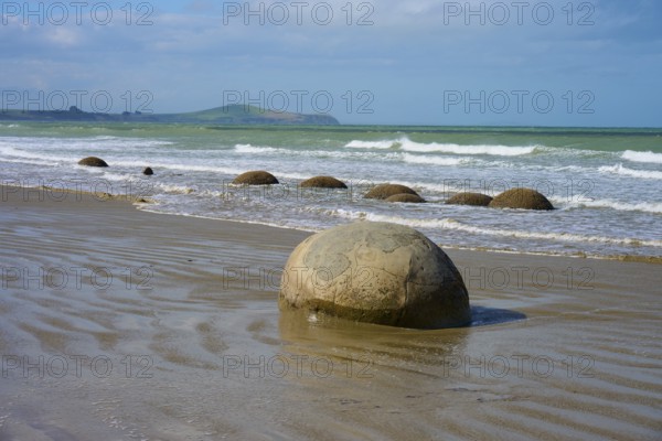 Große runde Felsen am Strand mit Wellen im Hintergrund und blauem Himmel, Moeraki Boulders,