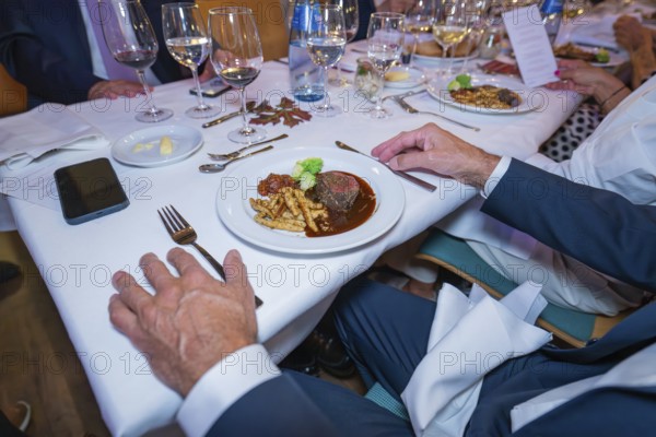 Steak with vegetables and pasta in an elegant table setting with white wine glasses and cloth