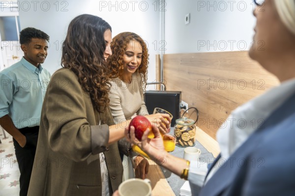 Coworkers gathering around a counter, offering an apple and orange juice, fostering team building