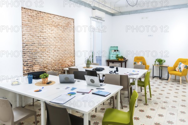 Bright open plan coworking office space featuring long white tables with laptops and charts, a