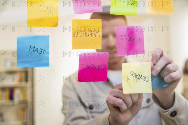 Red haired man organizing colorful sticky notes with handwritten words about planning, team, and
