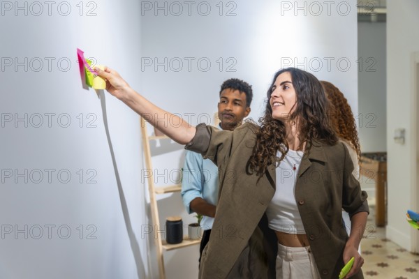 Diverse team collaborating, standing in a modern office, a smiling woman adding colorful sticky