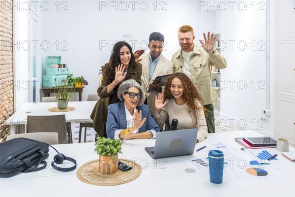 Diverse business colleagues smiling and waving at a laptop during a video call, connecting with