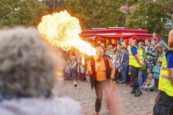 A fire-eater performs an exciting show in front of a large audience on a cobbled street,