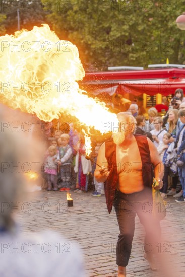 A man breathes fire during a show, surrounded by an attentive audience at a festival, Feuernacht,