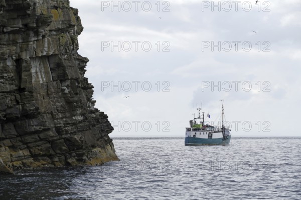 Turquoise boat on open sea near rocky cliffs, cloudy sky, Isle of Noss, Shetland Islands, Scotland,
