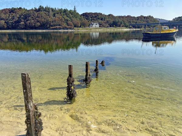 Shoreline landscape with clear water and a yellow boat, calm atmosphere, Silver Sands of Morar,