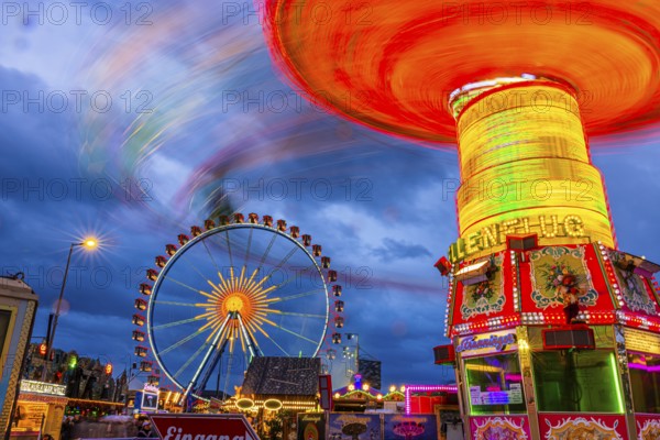 Illuminated chain carousel in motion, behind the Ferris wheel at standstill, Festwiese,