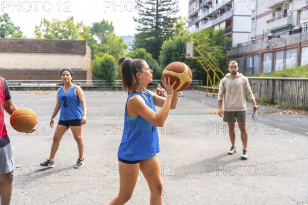 Concentrated female basketball player in blue uniform shooting ball during training outdoors on a
