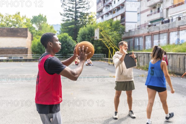 Young basketball player practicing shooting technique on outdoor court, receiving guidance from