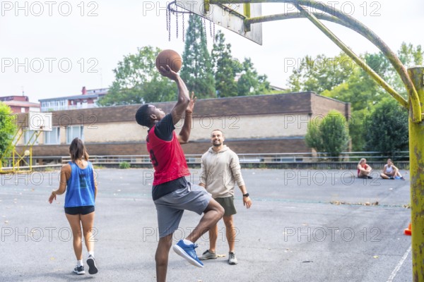 Group of friends enjoying a game of basketball on an outdoor court, with a young man shooting the