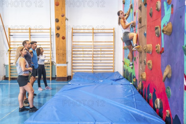Determined sportswoman practicing bouldering in a climbing gym, ascending a vibrant wall as friends