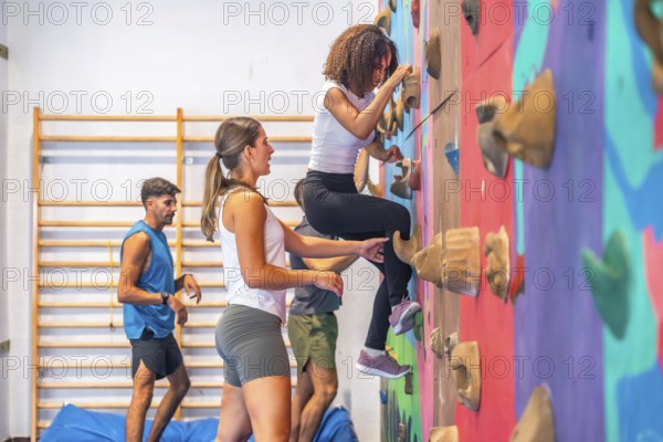 Young woman is practicing sport climbing on a colorful climbing wall in a gym, her instructor is