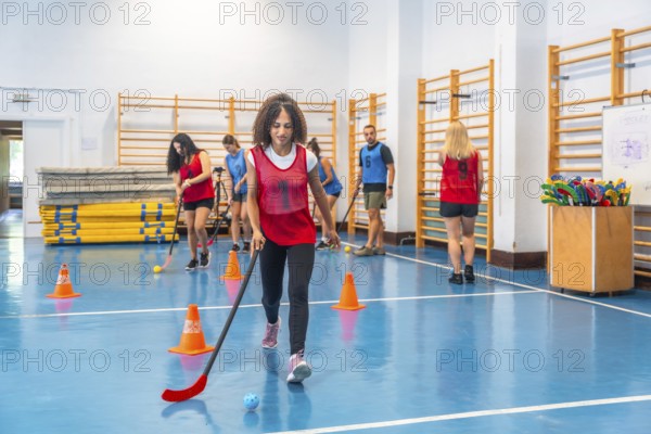 Young woman practicing floor hockey, dribbling the ball with her stick, during a training session