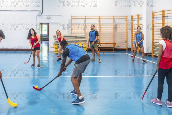 Floorball team players practicing passes during training inside a gym, skillfully hitting the ball