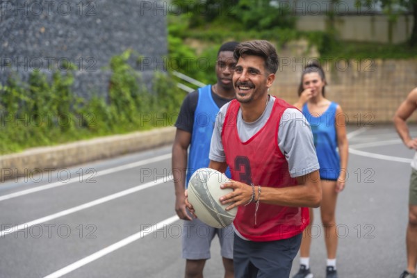 Rugby player wearing a red training bib smiling while holding the ball during a lively training