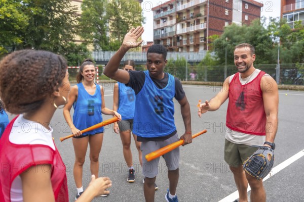 Group of cheerful multi ethnic friends wearing sportswear giving high fives and holding bats while