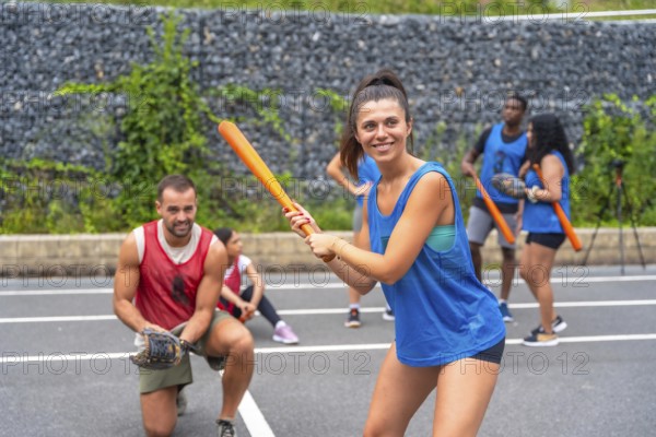 Smiling sportswoman holding an orange baseball bat, getting ready to hit the ball during a friendly