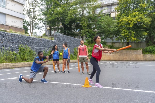 Group of friends enjoying a lively game of baseball on an outdoor court, with a woman swinging an
