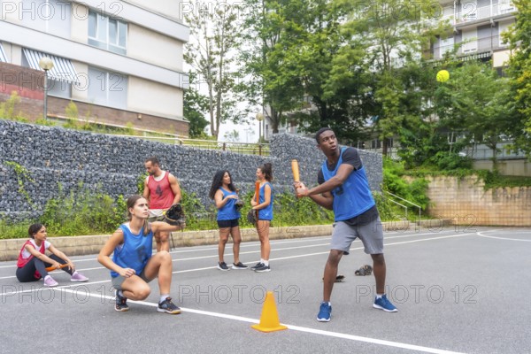 Group of young friends playing baseball in an urban environment, with a male player hitting the