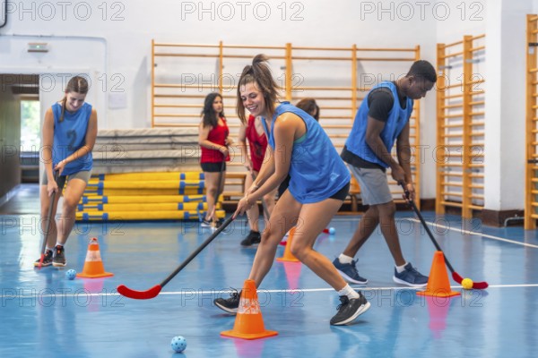 Female and male athletes wearing blue t shirts are practicing floorball, dribbling with sticks