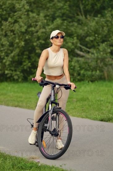 A woman enjoys a leisurely ride on her bicycle along a paved path in a vibrant green park. She
