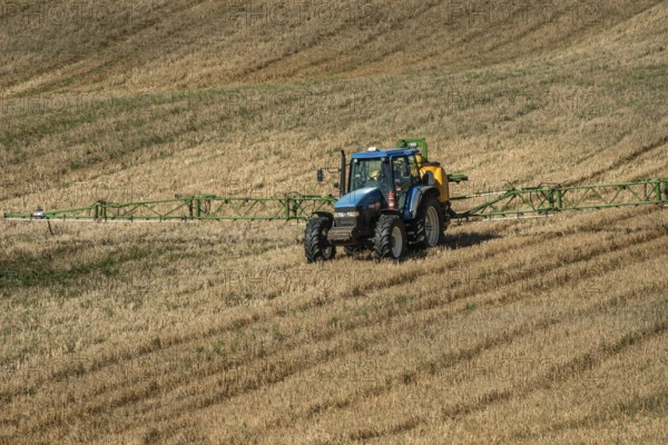 Tractor spreading fertilizer on harvested stubble field in Ystad municipality, Skåne county,