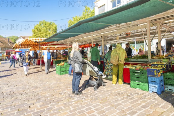 People stroll between market stalls with boxes full of goods under colourful umbrellas,