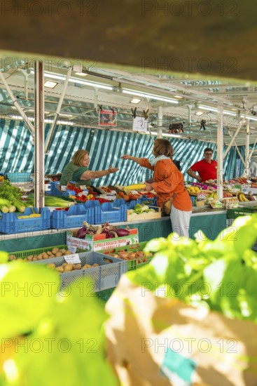 Market scene with lively exchange between customers and vendors at a colourful vegetable stand,