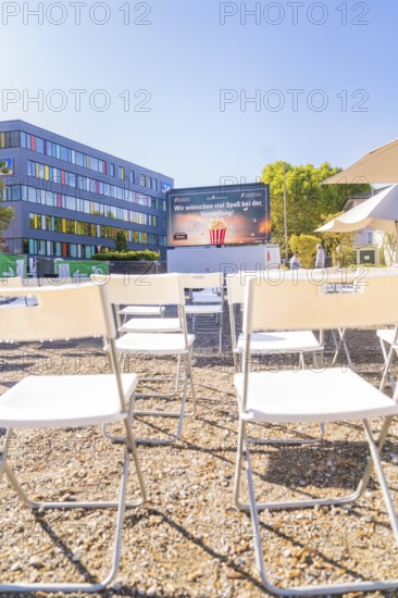 White chairs stand in rows in front of an outdoor screen on a sunny day, open air cinema