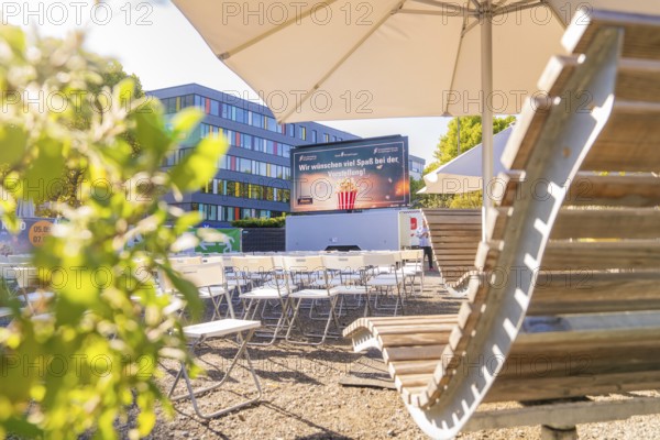Rows of chairs under parasols in front of a screen, enlivened by sunshine, open air cinema