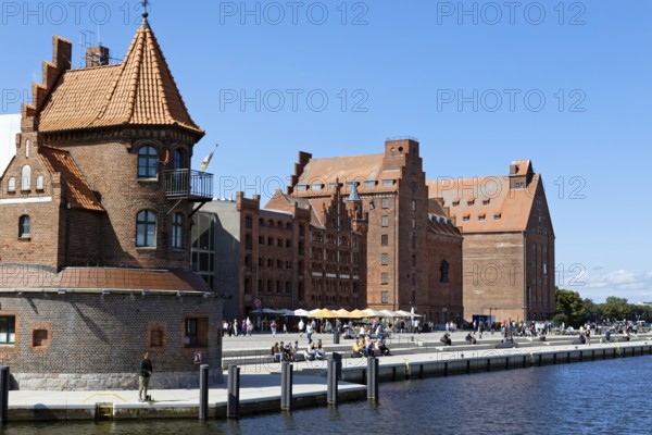 Visitors strolling and sitting on the waterfront promenade, building on the left two-storey brick