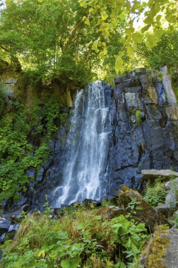 Vaucoux waterfall cascades gracefully over dark rocks, surrounded by lush greenery, Auvergne