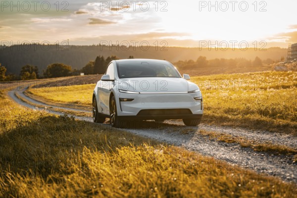 White car on a gravel road through a golden meadow at sunset, Tesla Model Y Juniper, electric car
