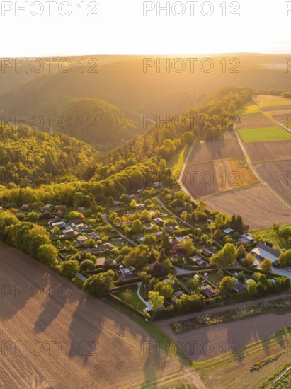Campsite nestled between fields and wooded hills in the warm sunset light, small town of Perle