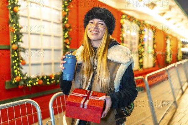 Young woman enjoying christmas spirit at a decorated outdoor market, holding a christmas present